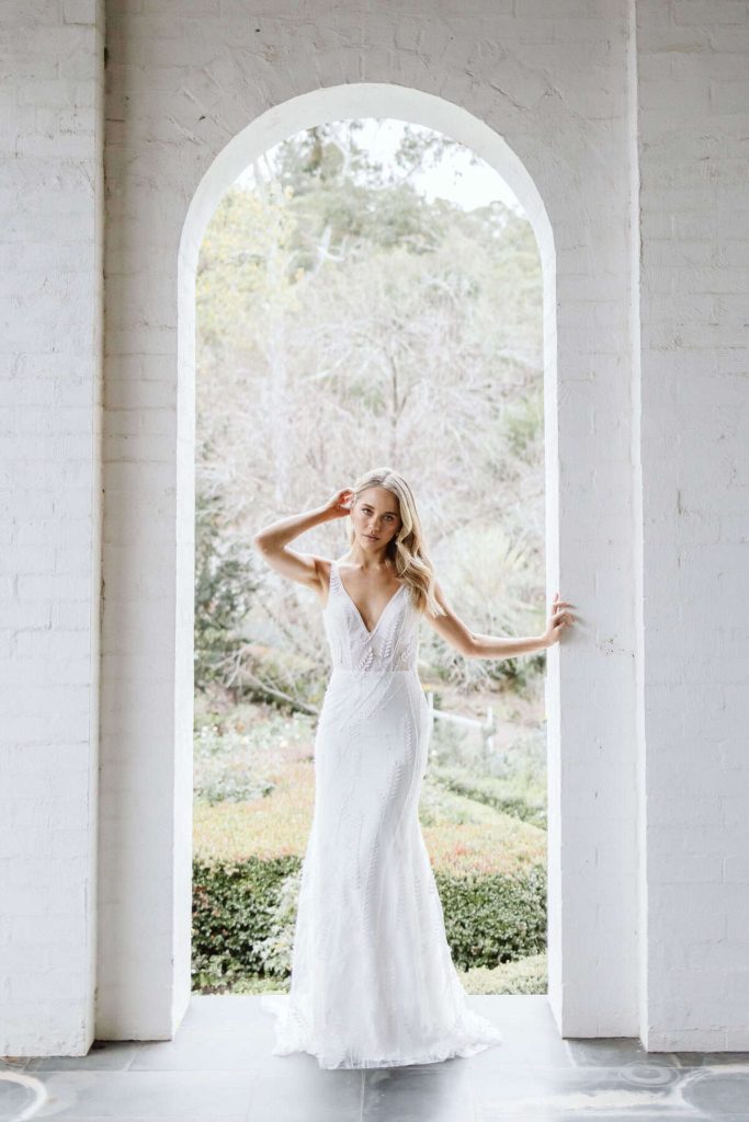 V-neck beaded sheath wedding gown in a white arched doorway