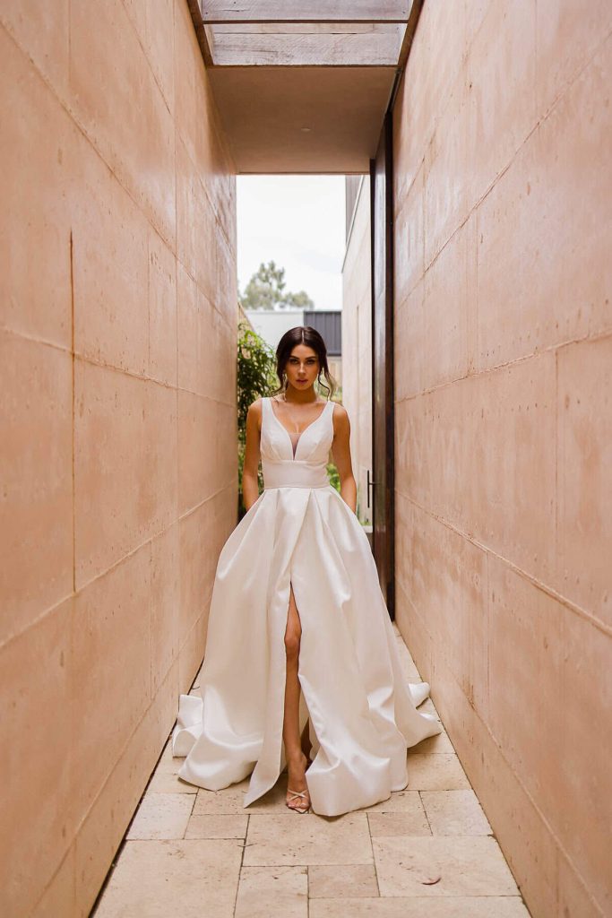 V-neck satin A-line wedding gown with thigh slit and full skirt by Elysian Bridal