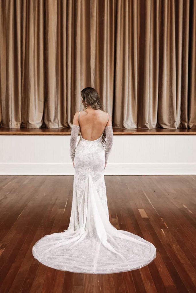 Open-back beaded lace fitted wedding gown with lace gloves by Zavana Bridal